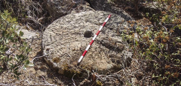 Rueda de molino con un jalón de escala. Fotografiada durante prospección arqueológica