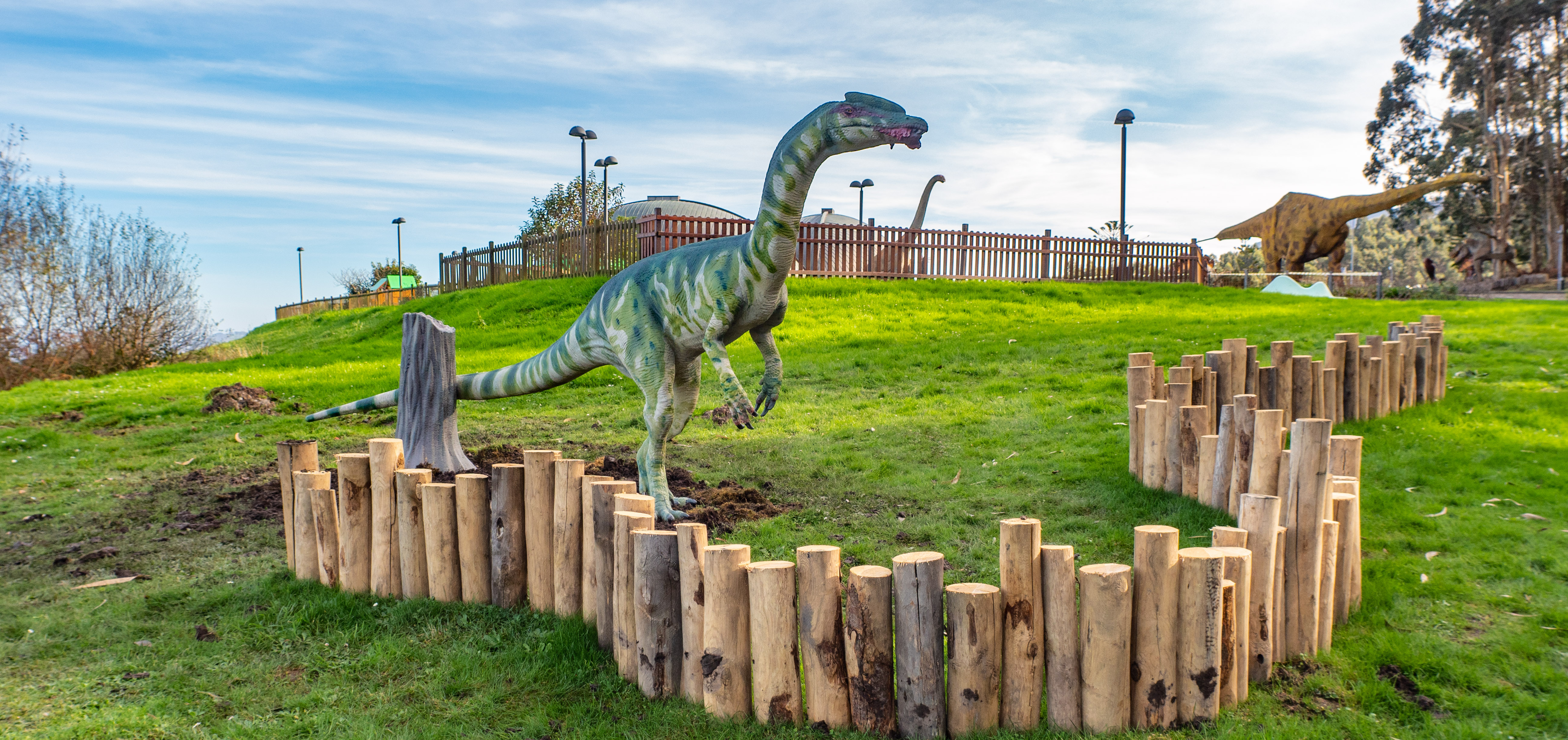 Reproducción del dinosaurio Liliensternus en el jardín exterior del Museo del Jurásico de Asturias. Es un dinosaurio terópodo (carnívoro) con un patrón de manchas de color verde, esbelto y con cresta. En la boca tiene un pedazo de carne.