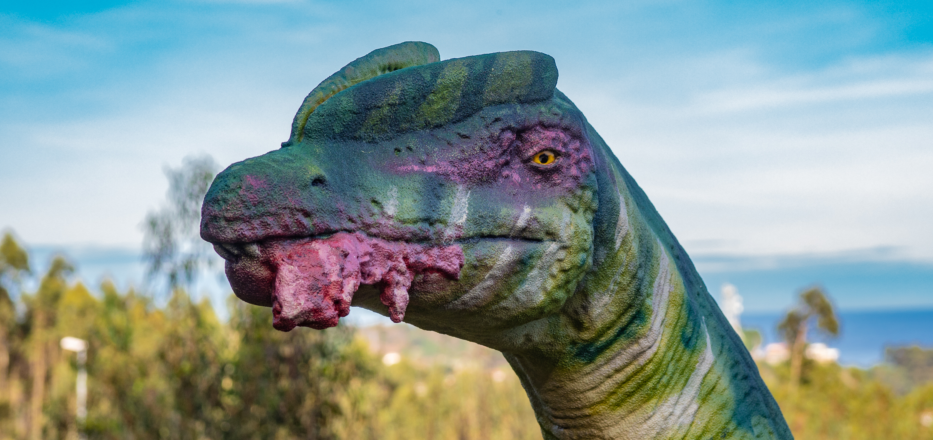 Detalle de la cabeza del dinosaurio Liliensternus. Tiene manchas rayadas verdes, una cresta, la mirada afilada y un pedazo de carne en la boca.